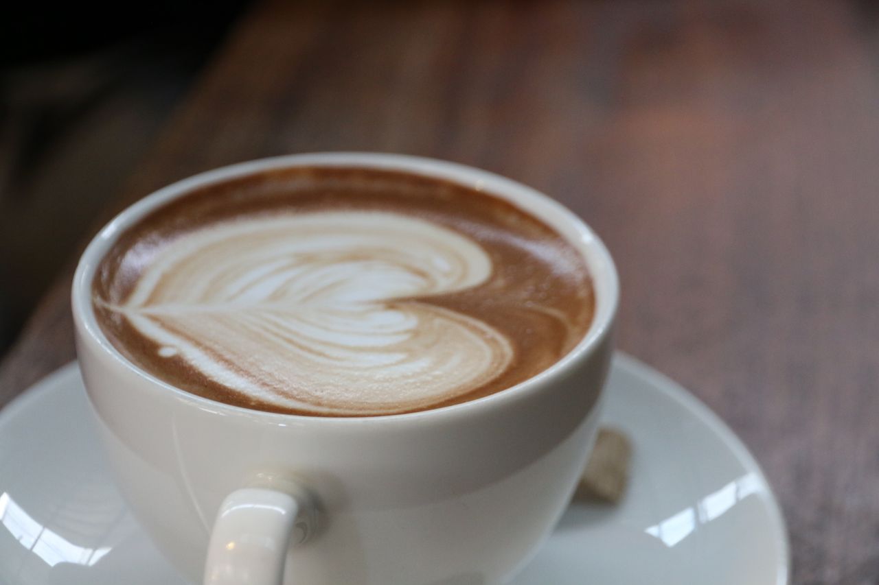 Close-up of a latte with heart-shaped art in a white cup on a wooden table.