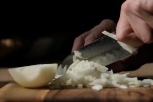 A person skillfully slices onions with a knife on a wooden board in a kitchen setting.
