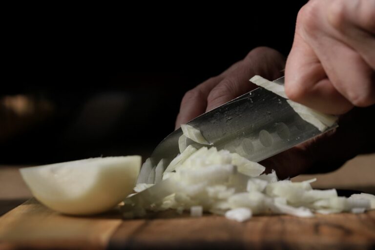A person skillfully slices onions with a knife on a wooden board in a kitchen setting.